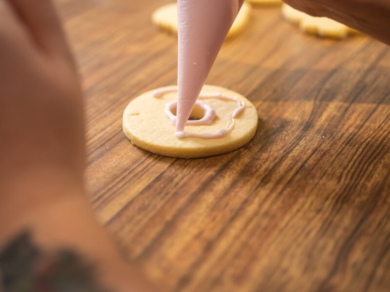 A person piping royal icing onto a round cookie.